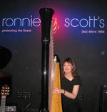 Carol Robbins poses with harp beneath sign for Ronnie Scott's in London.