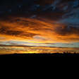 Dark and moody orange-streaked sunset over dark landscape.