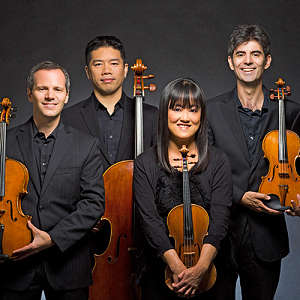 photo of four musicians holding their classical music instruments, three men and one women, each with a violin or cello