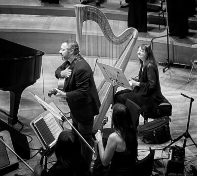 Larry koonse bows with hand on heart as carol robbins looks on, both on stage at walt disney concert hall november nineteenth, twenty-twenty-three.